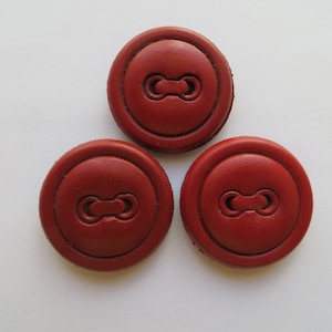 May include: Three circular red buttons arranged in a triangle formation. Each button features a smooth, matte surface with a raised outer rim and a central recessed horizontal slot with two circular holes for threading, creating a uniform appearance.