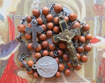 May include: A vintage rosary with brown wooden beads and silver-toned metal accents. The rosary features a crucifix with a detailed depiction of Jesus, a smaller cross, and a medal with an image of a saint. The background is a vintage illustration.