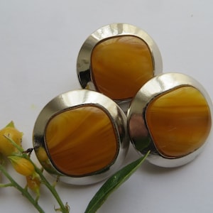 May include: Three vintage earrings with a silver-tone metal frame and a square, amber-colored center. The earrings are set against a white background with a sprig of yellow buds and green leaves.