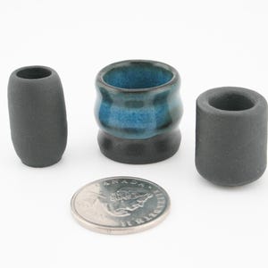 Peut inclure: Trois petites pièces en céramique dans les tons de gris et de bleu. L'une est un cylindre haut et arrondi, une autre est un cylindre court et arrondi, et la troisième est un petit récipient rond avec un intérieur bleu. Une pièce de monnaie est à côté des pièces.