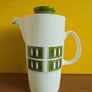 May include: White ceramic coffee pot with a green lid and green geometric pattern. The pot has a handle and a spout.