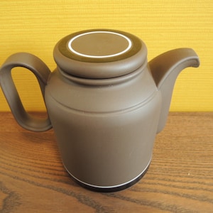 May include: A brown ceramic teapot with a lid and a green and white stripe around the top.