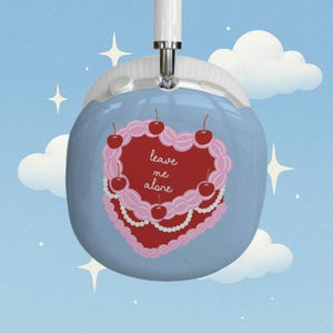 May include: Light blue over-ear headphones with a decorative heart-shaped cake design. The cake is red with pink frosting, cherries, and the text "leave me alone". The background is a blue sky with clouds and stars.