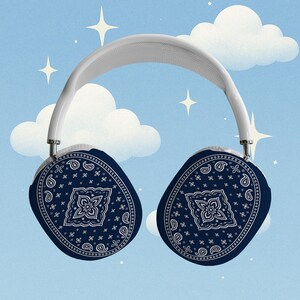 May include: White and silver over-ear headphones with navy blue paisley earcups. The earcups feature a classic bandana pattern with a central floral design. The background is a light blue sky with white clouds and stars.