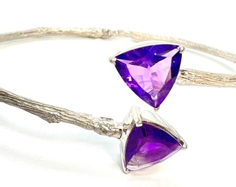 May include: A silver bangle bracelet with a twig-like design features two triangular amethyst gemstones.