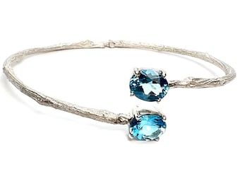 May include: A silver bangle bracelet with a twig-like design and two oval-shaped blue topaz gemstones.