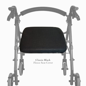Puede incluir: Una funda de asiento de forro polar negro colocada en un andador con cuatro ruedas y respaldo curvo. El texto Classic Black Fleece Seat Cover est&aacute; impreso debajo del asiento. El marco del andador es negro con un asa acolchada.