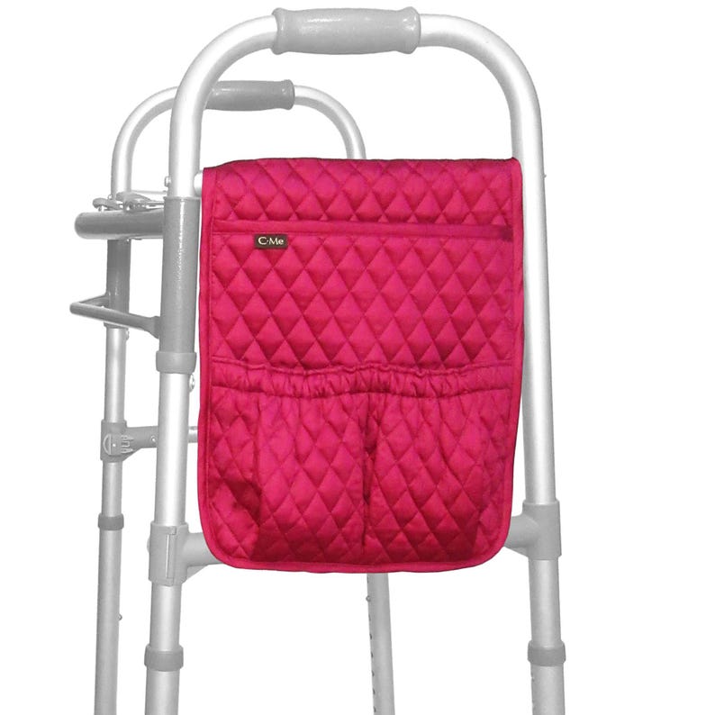 May include: A fuchsia walker bag with a quilted diamond pattern. The bag has a zippered top pocket and two lower open pockets. The bag is attached to a silver walker frame. The bag has the text "C Me".