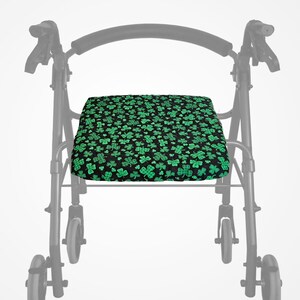 May include: A black and green patterned seat cushion for a walking frame. The cushion displays a repeating pattern of green shamrocks on a black background. The walking frame is a standard model with wheels and handles.