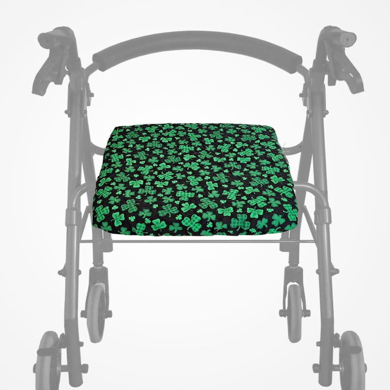 May include: A black and green patterned seat cushion for a walking frame. The cushion displays a repeating pattern of green shamrocks on a black background. The walking frame is a standard model with wheels and handles.