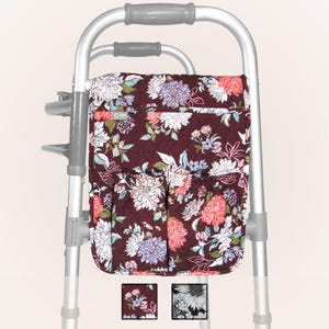 May include: A floral patterned walker bag with multiple pockets. The bag is attached to a silver walker. The bag is quilted and has a zipper closure. The bag is available in two colors: burgundy with white and pink flowers and black with white flowers.