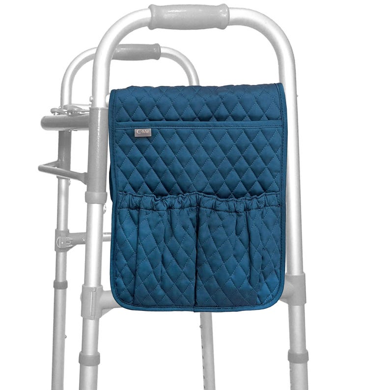 May include: A teal quilted walker bag with two front pockets and a small label. The bag is attached to a silver walker. The bag has a diamond pattern and is designed to hold personal items.