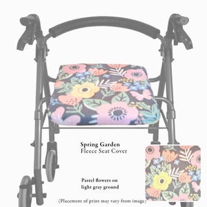 Puede incluir: Un andador de metal negro con una funda de asiento de forro polar con estampado Spring Garden. La tela muestra flores y hojas en tonos pastel sobre un fondo gris claro. El texto dice: Spring Garden Fleece Seat Cover, Pastel flowers on light gray ground, y Placement of print may vary from image.