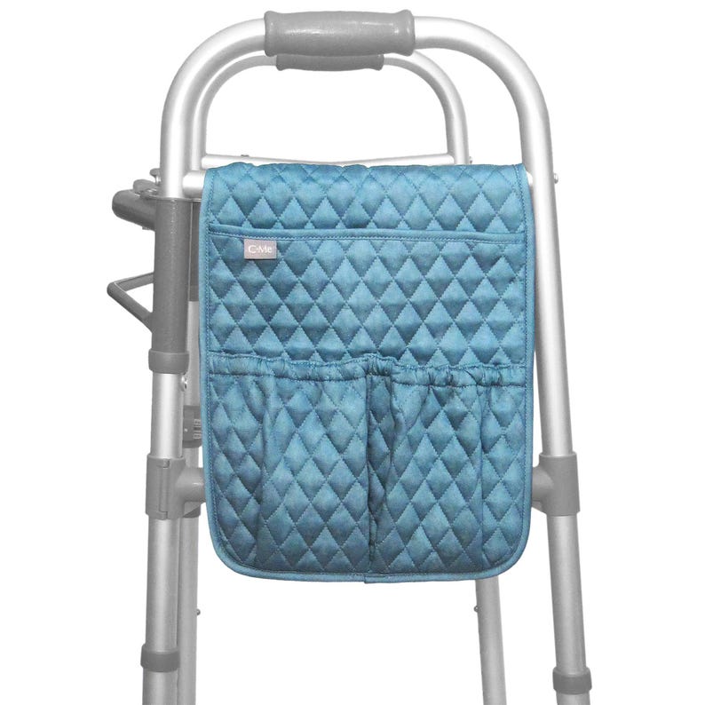 May include: A teal quilted walker bag with two front pockets and a diamond pattern. The bag is attached to a silver walker frame, providing convenient storage for personal items.