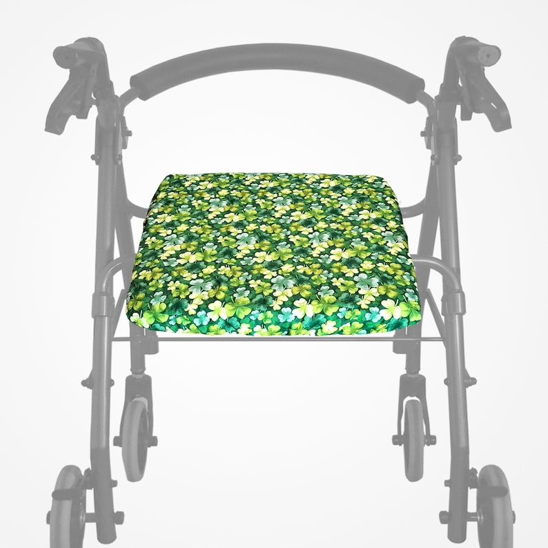 May include: A walker seat cushion featuring a pattern of green and yellow clovers. The cushion is rectangular and designed to fit a walker frame. The clover design uses various shades of green and yellow.