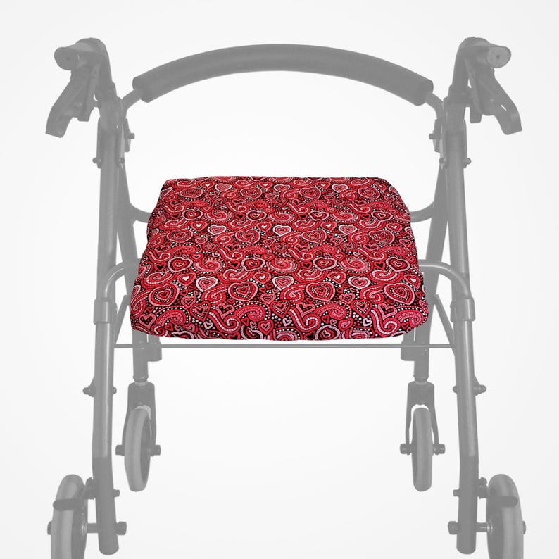 May include: A red and white heart-patterned seat cushion for a walker. The cushion is rectangular and features a repeating design of hearts and paisley shapes. The walker frame is visible in the background.