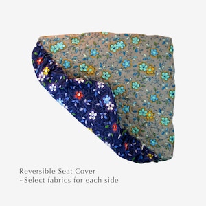 May include: Reversible seat cover with a floral pattern on both sides. One side is a dark blue fabric with white, red, and yellow flowers. The other side is a light gray fabric with blue, yellow, and orange flowers. "Reversible Seat Cover - Select fabrics for each side" is written below the image.