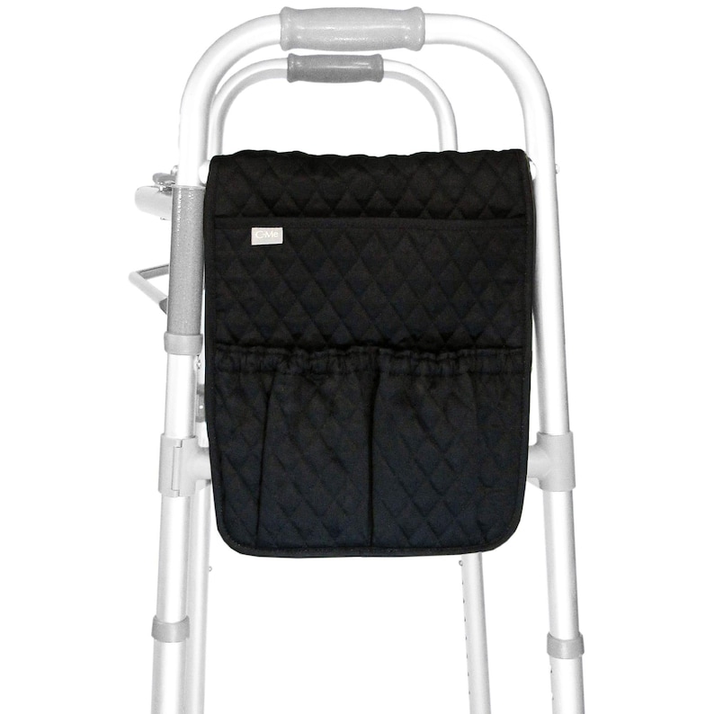 May include: Black quilted walker bag with two front pockets and a small label. The bag is attached to a silver walker frame. The bag has a diamond pattern.