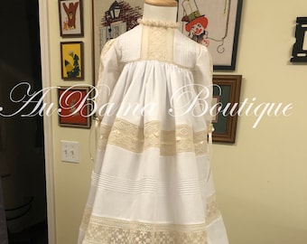 Könnte beinhalten: Weißes Taufkleid mit Spitzenbesatz und Rüschen am Saum. Das Kleid ist auf einer Kleiderpuppe und hat einen hohen Ausschnitt.