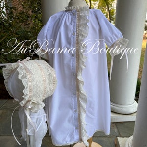 May include: White baby gown with a lace trim and a matching bonnet. The gown has a button closure and a ruffle down the front. The bonnet has a lace trim and a ribbon tie.