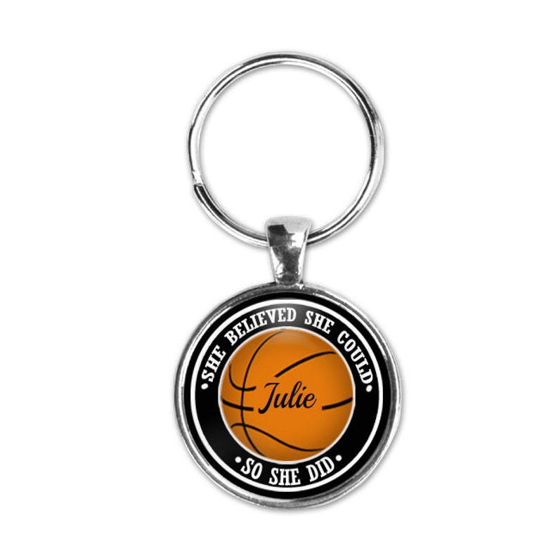 May include: A silver keychain with a round black and white charm featuring a basketball with the text "She Believed She Could. So She Did." and the name "Julie" on the basketball.
