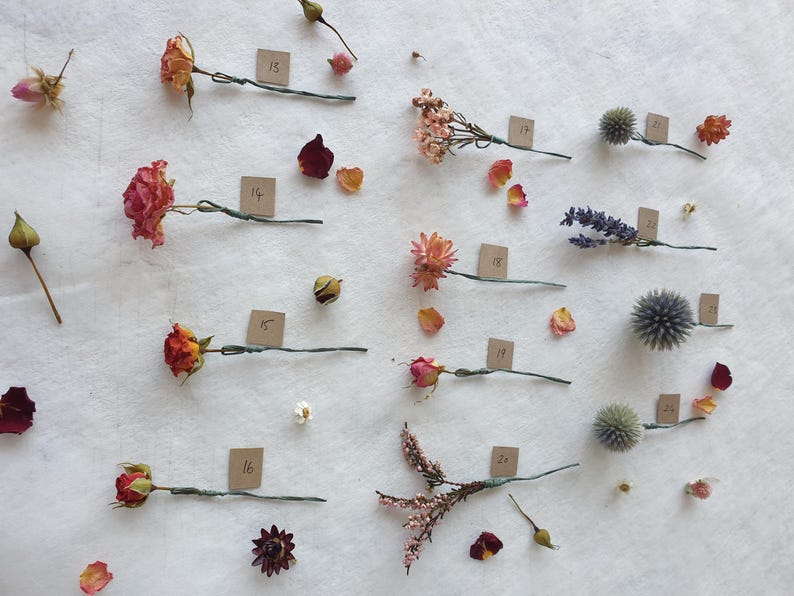 May include: Assortment of dried flowers and plants, including roses, lavender, and thistle, arranged on a white surface with numbered tags.