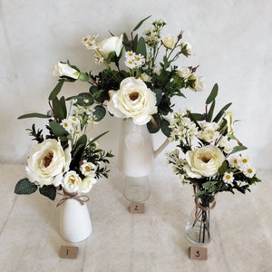 May include: Three white ceramic vases with white flower arrangements. The vases are different shapes and sizes. The flowers are all white and have a variety of textures. The vases are numbered 1, 2, and 3.