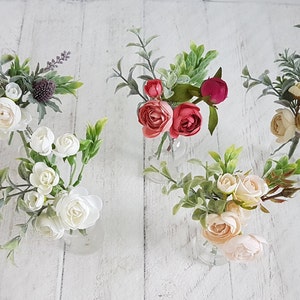 May include: Five small bouquets of artificial flowers in clear glass vases. The bouquets include white, pink, red, and green flowers.