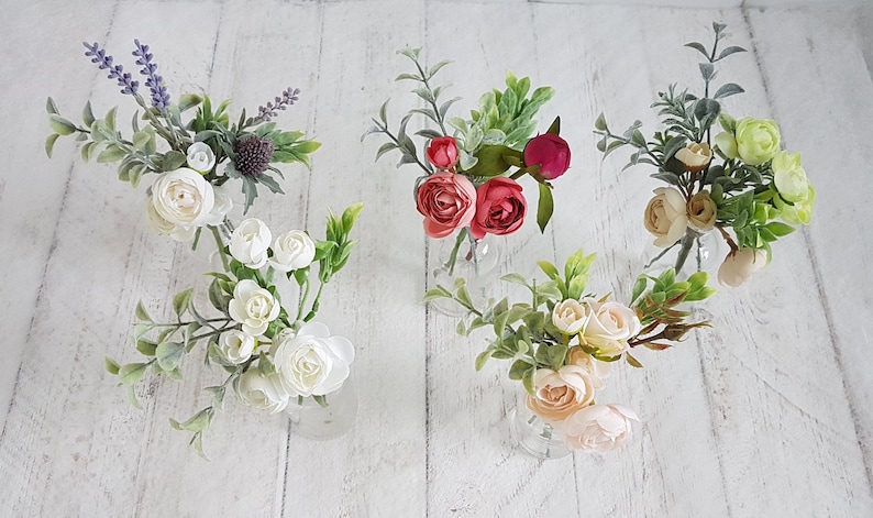 May include: Five small bouquets of artificial flowers in clear glass vases. The bouquets include white, pink, red, and green flowers.