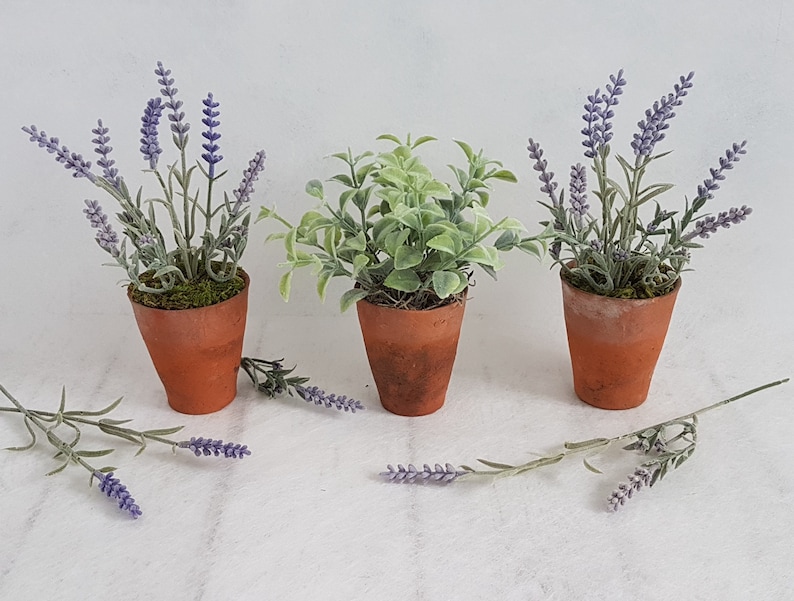 May include: Three terracotta pots with faux plants. Two pots contain lavender plants with purple flowers and green leaves. The third pot contains a green leafy plant.
