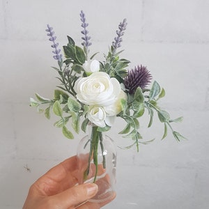 May include: A small bouquet of white flowers and lavender in a clear glass bottle. The flowers are arranged in a simple, elegant style.