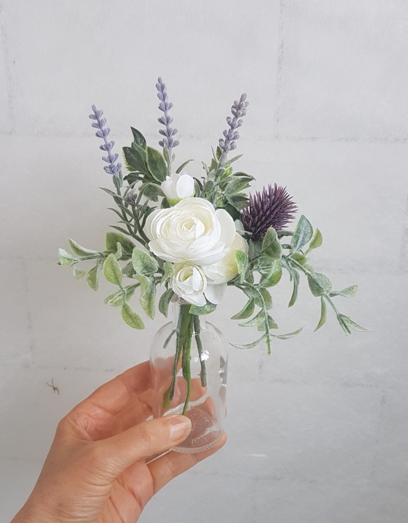May include: A small bouquet of white flowers and lavender in a clear glass bottle. The flowers are arranged in a simple, elegant style.