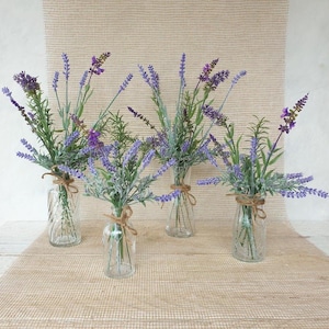 May include: Five clear glass vases with rustic twine tied around the neck, each filled with a bouquet of purple lavender flowers.
