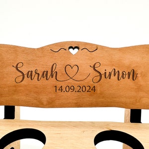 May include: A wooden bench with a personalised sign that reads "Sarah & Simon 14.09.2024". The sign has a heart design and is engraved with the couple's names and wedding date.