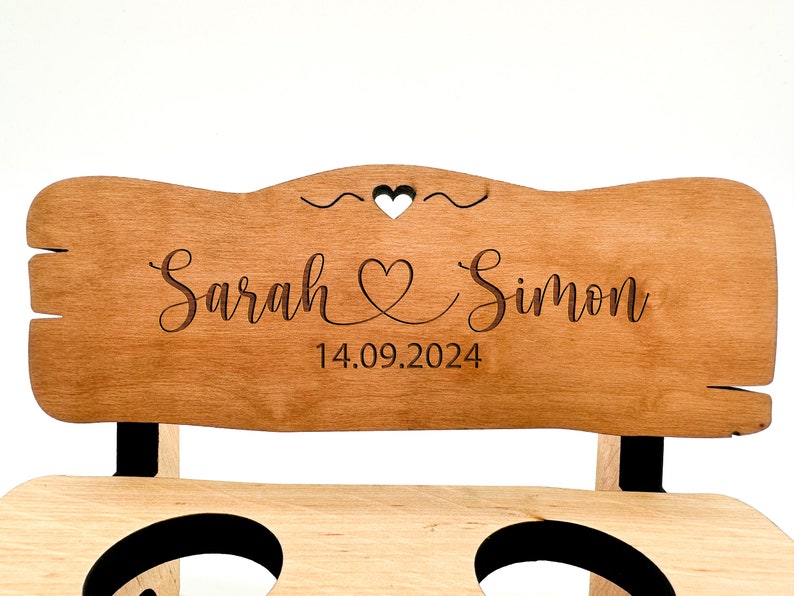 May include: A wooden bench with a personalised sign that reads "Sarah & Simon 14.09.2024". The sign has a heart design and is engraved with the couple's names and wedding date.