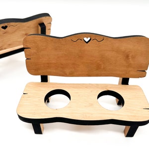 May include: A wooden bench with a heart cutout in the back, painted black with a white heart. The bench has two round cutouts in the seat, perfect for holding eggs.