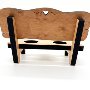 May include: A wooden bench with a heart-shaped cutout in the back, two cup holders, and black painted accents.
