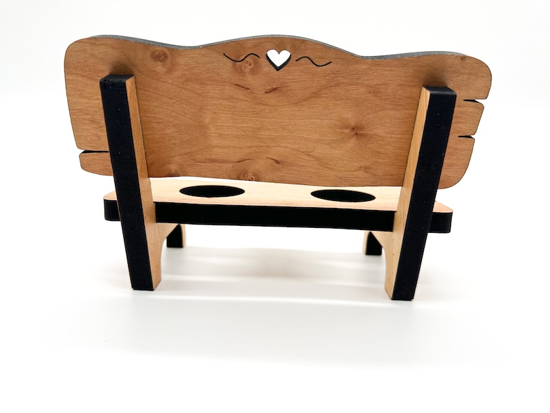 May include: A wooden bench with a heart-shaped cutout in the back, two cup holders, and black painted accents.