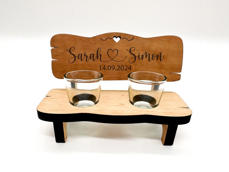 May include: Wooden wedding shot glass holder with two shot glasses. The holder is shaped like a bench and has a sign that says "Sarah & Simon 14.09.2024".