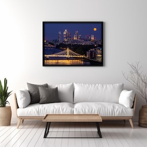 Può includere: Uno skyline notturno di Londra con la luna piena nel cielo. Lo skyline della città è illuminato da luci, e un ponte attraversa il Tamigi.