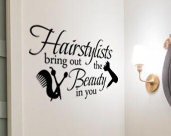 Può includere: Un bagno con un lavandino bianco e uno specchio rotondo con cornice nera. La parete ha un adesivo in vinile nero che recita "Hairstylists bring out the beauty in you".