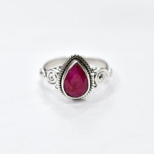 Puede incluir: Un anillo de plata con una piedra preciosa de rubí en forma de pera engastada en un engaste de plata decorativo.
