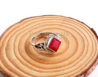 May include: A silver ring with a square red gemstone set in a decorative silver band. The ring is on a wooden surface.