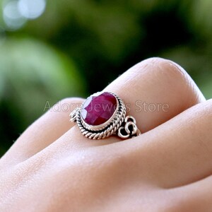May include: A silver ring with a red gemstone set in a twisted band. The ring is on a person's finger.