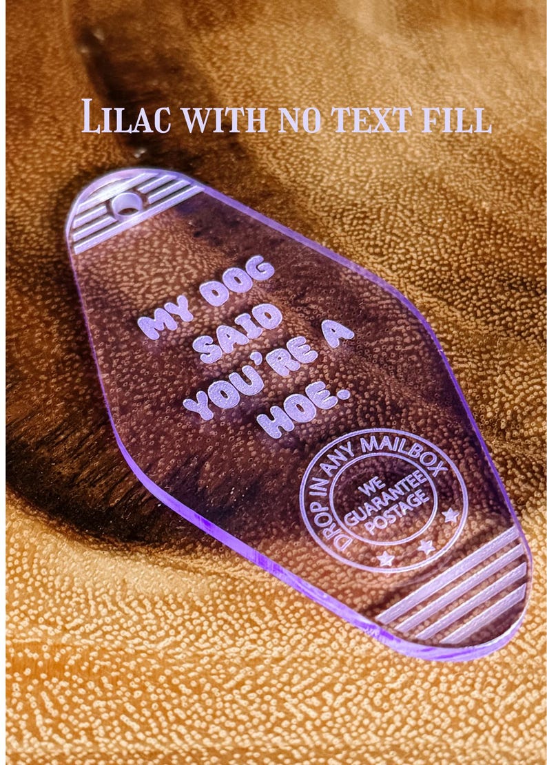 May include: A translucent lilac motel-style keychain with a rounded diamond shape. The text reads: MY DOG SAID YOU'RE A HOE. Below this, a circular emblem features the text: DROP IN ANY MAILBOX WE GUARANTEE POSTAGE. It has a hole at the top.