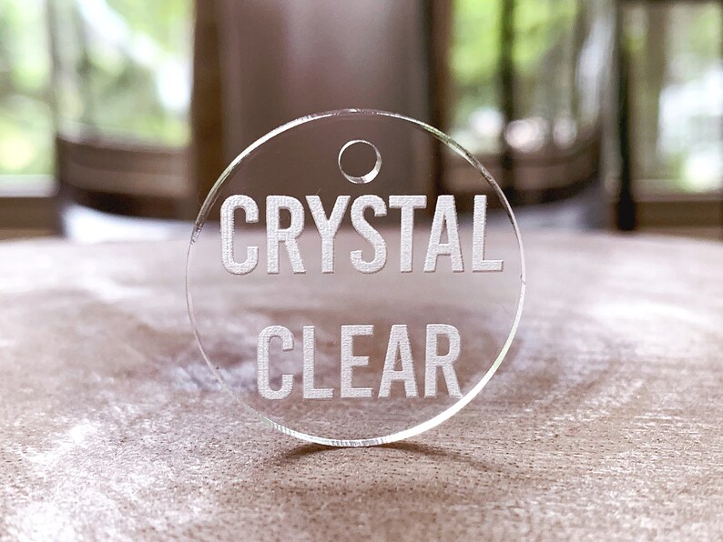 May include: A round, clear acrylic tag with a hole at the top. The tag has the words "CRYSTAL CLEAR" etched in white.