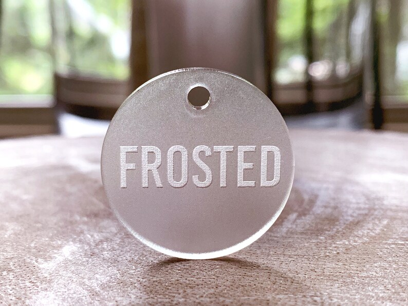 May include: A frosted white round tag with a hole at the top and the word "FROSTED" engraved in white.