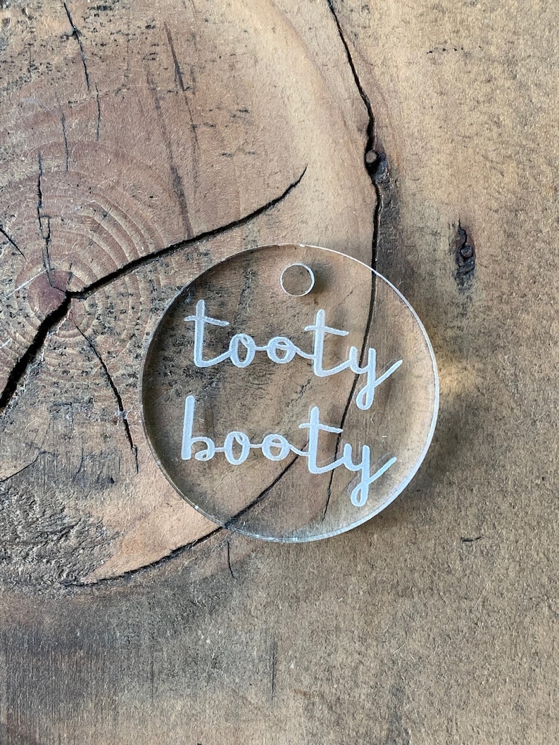 May include: A clear acrylic circle keychain with the text "tooty booty" written in white.
