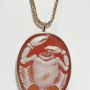 May include: A gold chain necklace with a cameo pendant featuring a carved white shell design of a crab on a red background.