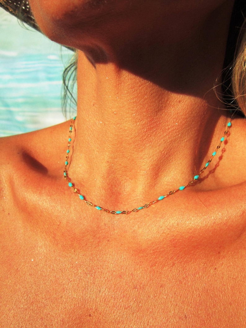 A close-up of a person's neck and chest area, with a necklace featuring turquoise beads visible.